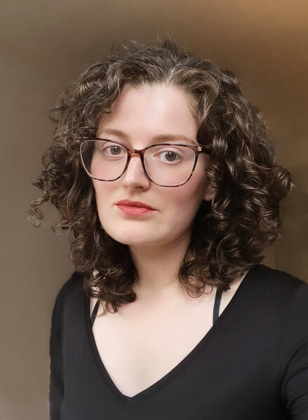 A white woman with curly brown hair and glasses wearing a black shirt