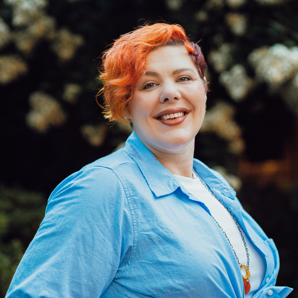 Woman with red hair and blue shirt is facing to the side and smiling to camera.
