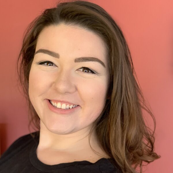 Tori's face against a red background. tori is a 30-year old white woman with dark hair and dark eyes, wearing a black shirt. tori is smiling.